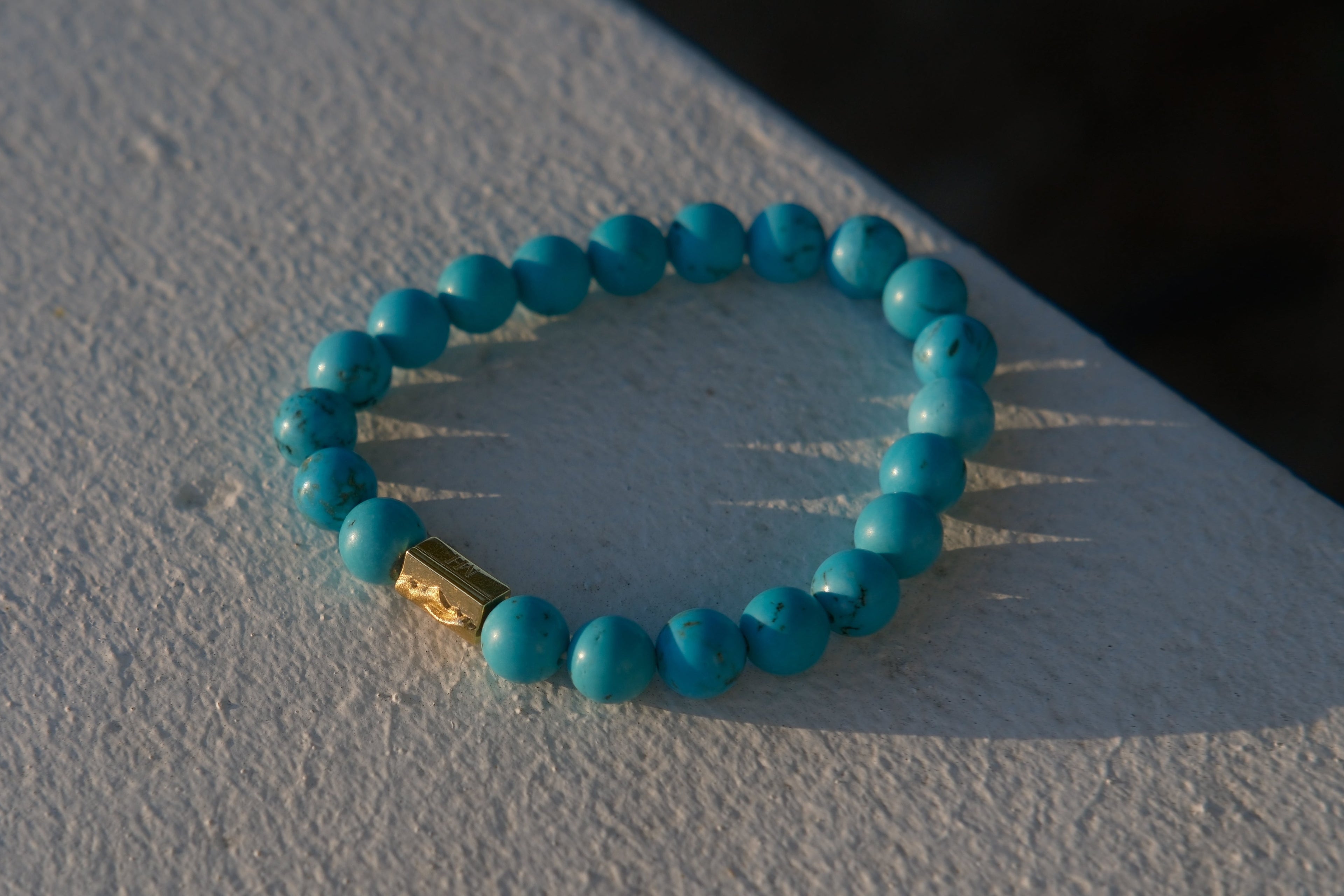 A turquoise beaded stretch bracelet with a small gold spacer bead, resting on a textured white surface.